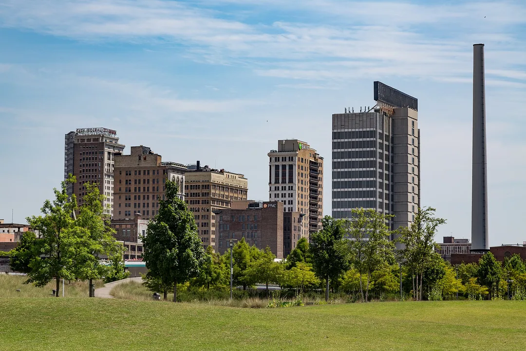Downtown buildings beyond a grassy park and young trees in Alabama.