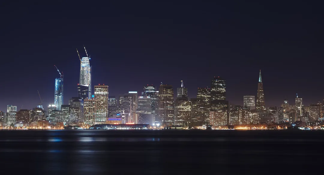 An illuminated California skyline stretches across dark water at night.