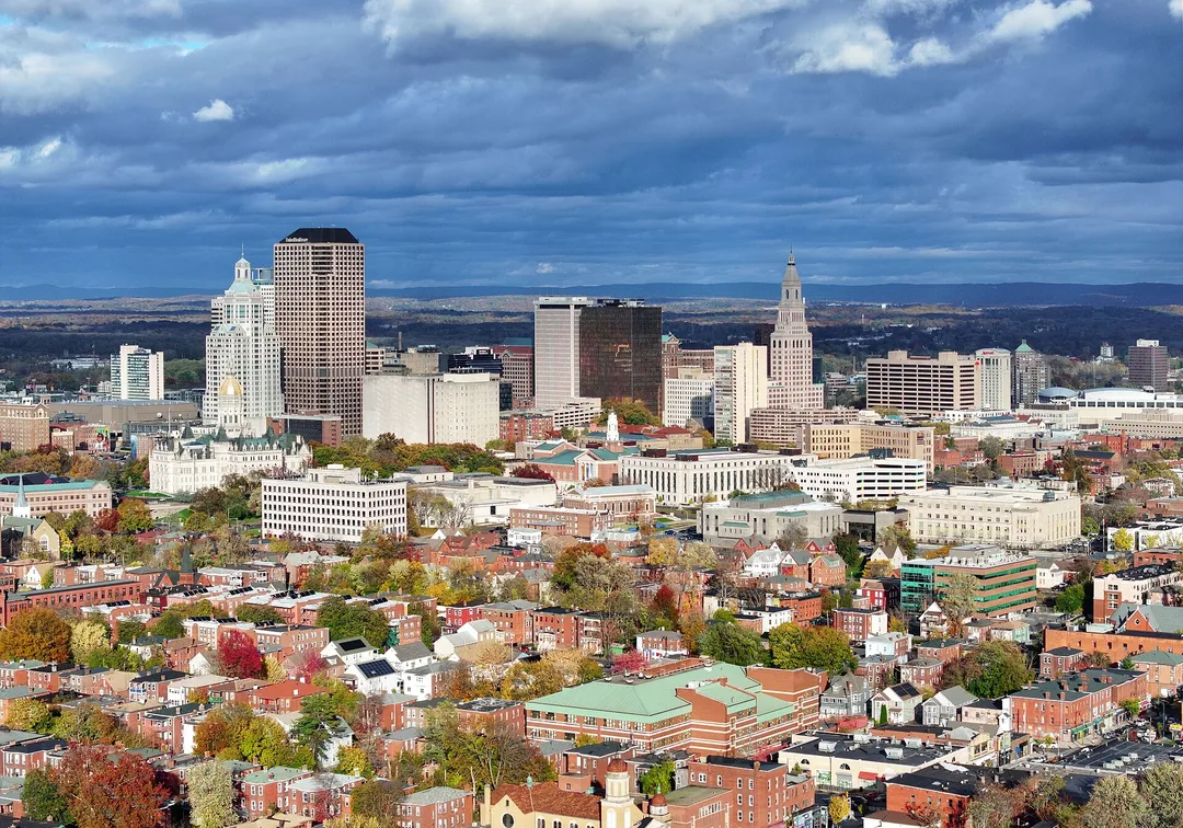 Dense Connecticut city blocks and downtown towers beneath dark clouds.