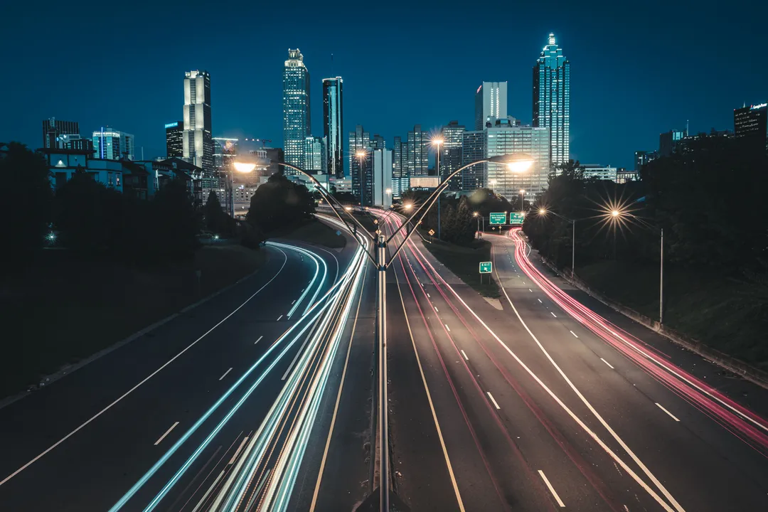 Streaks of headlights and taillights lead toward a Georgia skyline after dark.