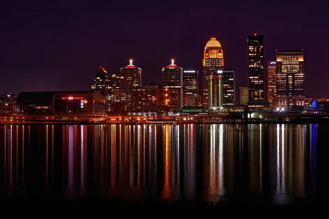 Warm city lights form long reflections on the water beside a Kentucky skyline.