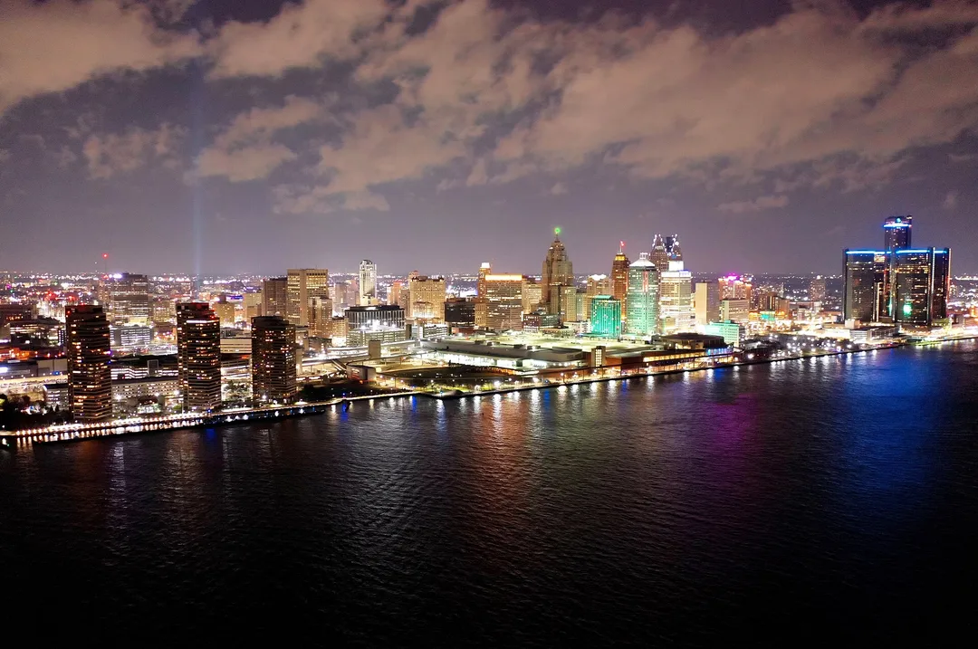 An illuminated Michigan waterfront curves beside a dark river under cloudy skies.