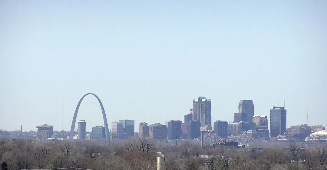 The Gateway Arch rises beside the St. Louis skyline beyond leafless trees.