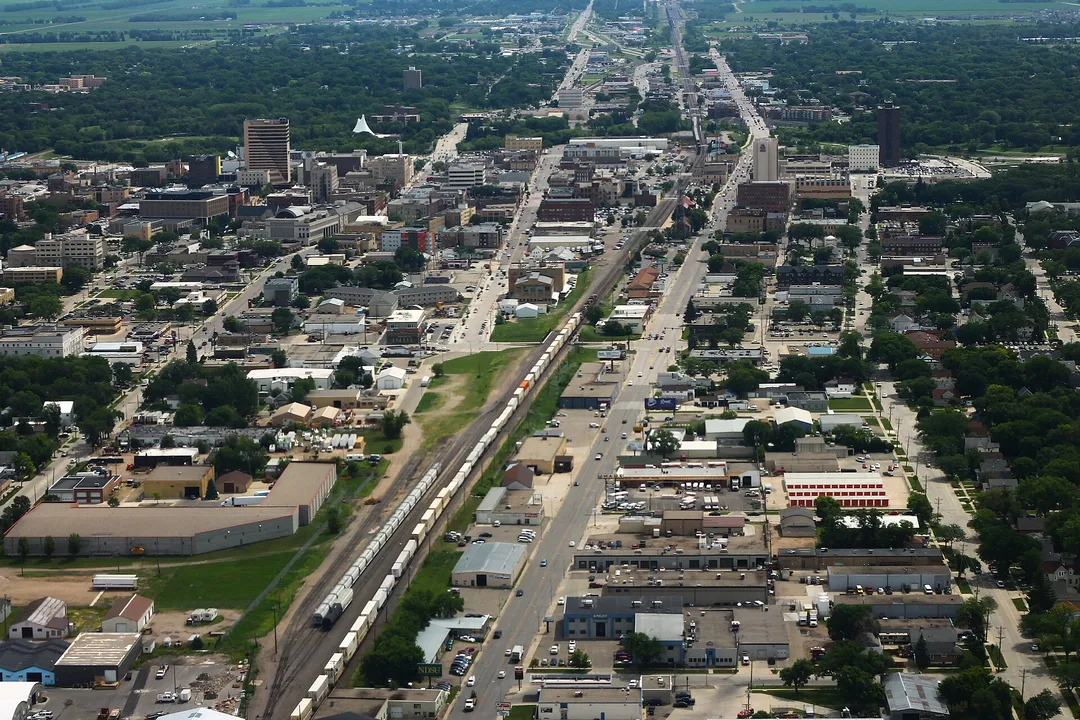 An aerial view of a railway corridor running between North Dakota city blocks and leafy neighborhoods.