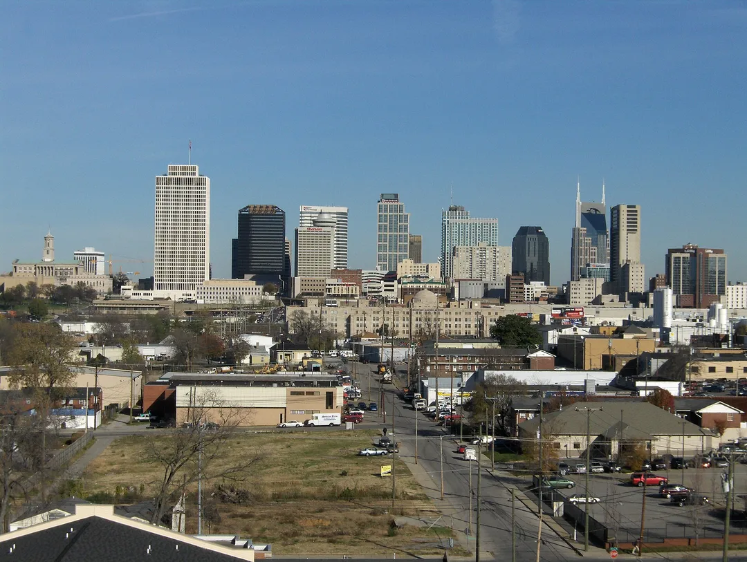 Tennessee downtown towers rise beyond low buildings, roads, and bare trees under a blue sky.