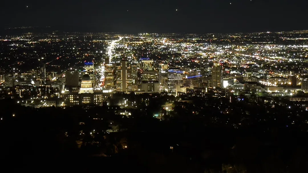 A grid of Utah city lights stretches toward the horizon beyond a dark hillside at night.