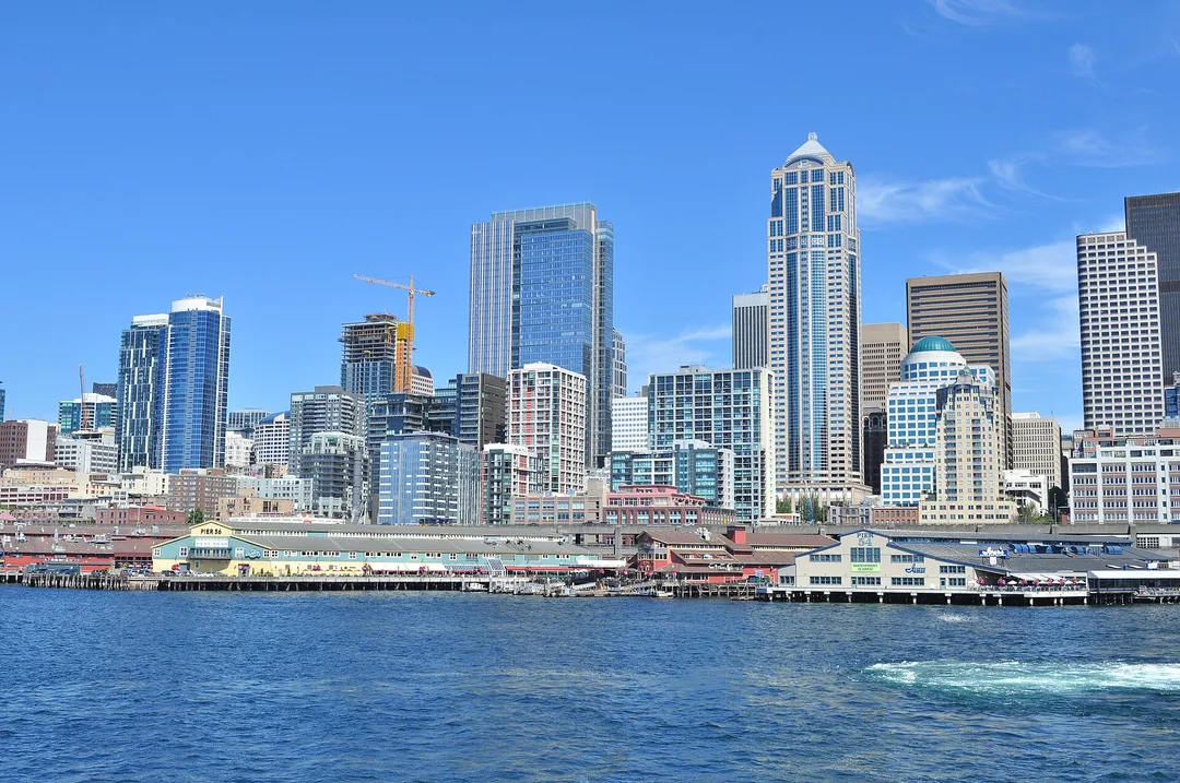 Washington waterfront buildings and downtown towers rise above bright blue water in the sunshine.