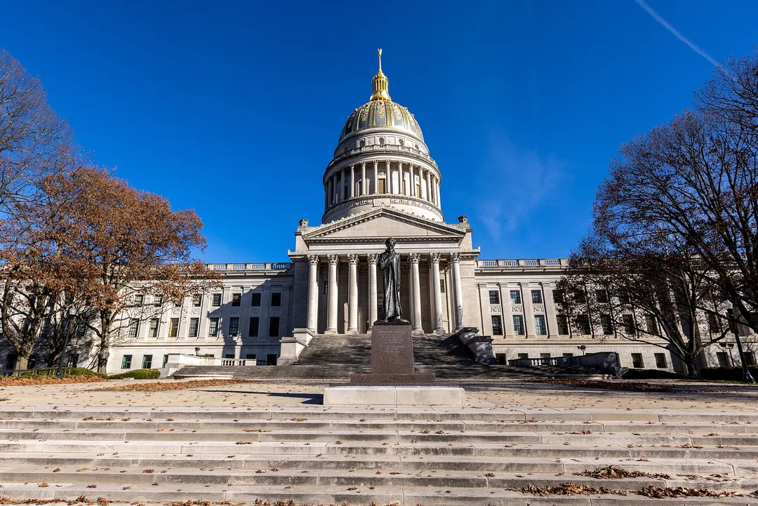 West Virginia's gold-domed capitol stands above broad stone steps between autumn trees.