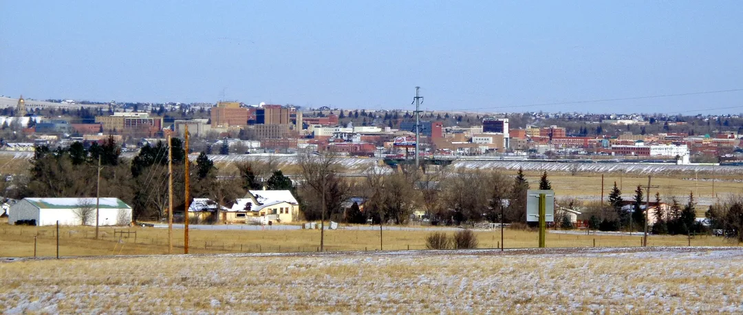 A field dusted with snow lies below scattered houses and distant city buildings in Wyoming.